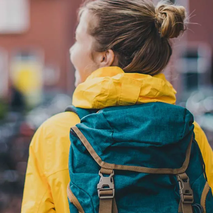 college student on campus in a yellow coat with green backpack not facing the camera