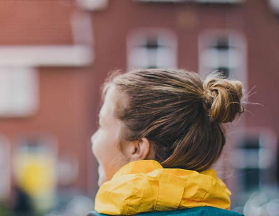 college student on campus in a yellow coat with green backpack not facing the camera